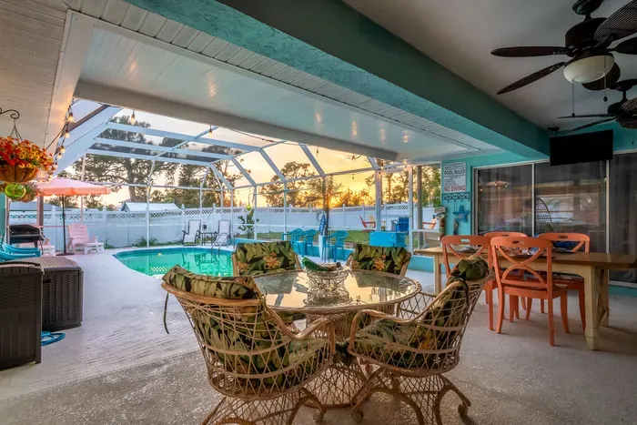 Dine in tropical comfort with this stylish indoor-outdoor patio area, featuring a glass-top rattan dining set and vibrant decor.