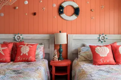 Unwind in this cheerful twin-bed room designed with beachy bliss in mind. The coral shiplap wall, nautical accents, and seashell-themed bedding make this space feel like a seaside escape.