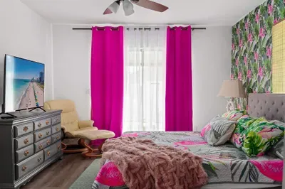 Step into paradise in this vibrant and cozy master bedroom! Featuring a plush king-sized bed with flamingo-themed bedding, a luxe tufted headboard, and a lush tropical accent wall, this space is your private oasis.