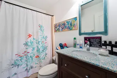 Fresh, fun, and full of coastal charm, this bathroom brings the beach indoors with a coral reef-themed shower curtain, a sea glass-inspired countertop, and playful ocean artwork.