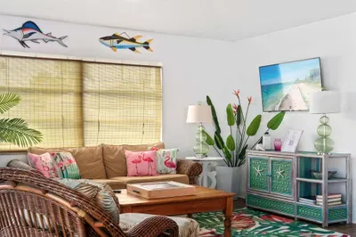 Kick back in this sun-drenched tropical living room, where island vibes meet comfort and style. Relax on plush wicker furniture, enjoy your favorite shows on the wall-mounted smart TV, and soak in the playful décor—complete with flamingo pillows.