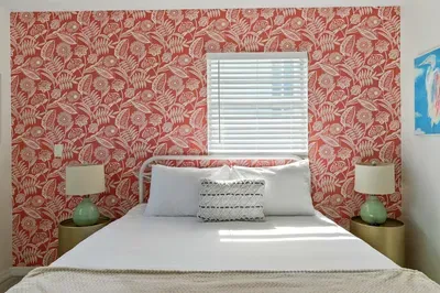 Sleep in style with a bold red floral accent wall framing a plush white bed. Paired with matching mint-green lamps and soft natural light, this bedroom is the perfect blend of charm, comfort, and coastal flair.