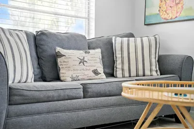 Cozy up on the plush gray sofa adorned with nautical-inspired pillows, bringing a touch of the seaside indoors. Perfect for relaxing with a book or sipping coffee, this inviting spot captures true coastal charm.