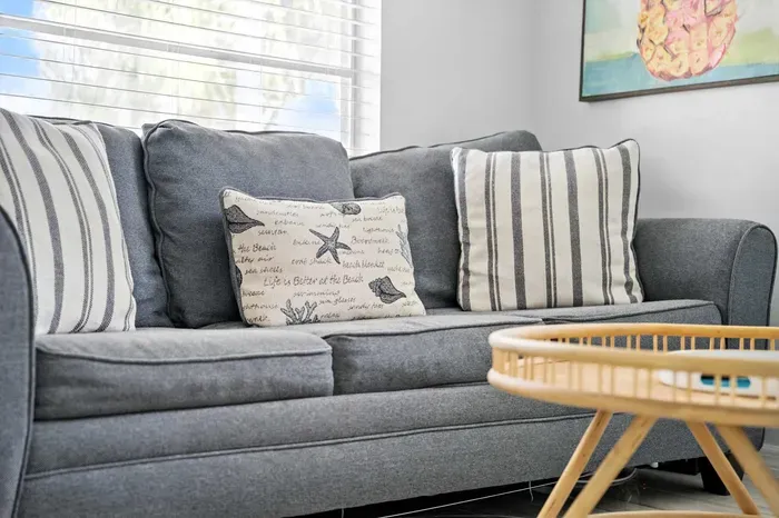 Cozy up on the plush gray sofa adorned with nautical-inspired pillows, bringing a touch of the seaside indoors. Perfect for relaxing with a book or sipping coffee, this inviting spot captures true coastal charm.