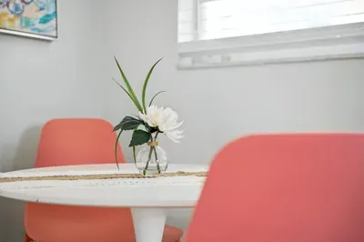 Enjoy morning coffee at this chic dining nook with vibrant coral chairs, a sleek white table, and a fresh floral touch. Sunlight pours in through the window, creating a bright and inviting space for meals or conversation.
