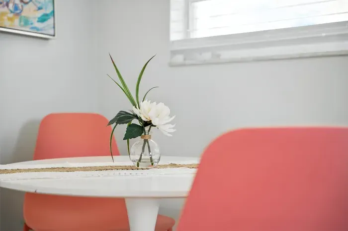 Enjoy morning coffee at this chic dining nook with vibrant coral chairs, a sleek white table, and a fresh floral touch. Sunlight pours in through the window, creating a bright and inviting space for meals or conversation.