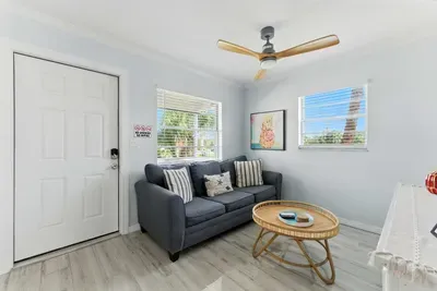 "Bright and welcoming living space with a comfy gray sofa, coastal-inspired pillows, and a chic rattan coffee table. Sunlight streams through large windows, creating the perfect spot to relax after a day at the beach.