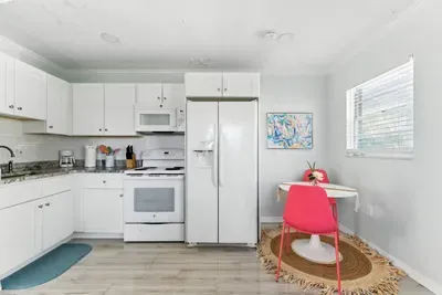 Bright and modern kitchen with crisp white cabinets, granite counters, and full-size appliances. A cozy dining nook with a pop of coral adds charm, making it perfect for enjoying meals after a day of coastal adventures.