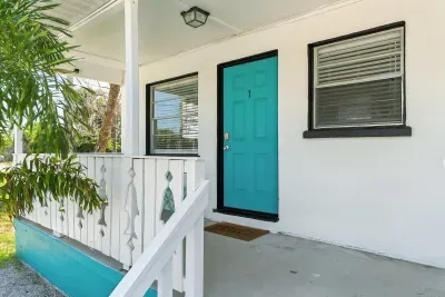 Step into your coastal escape through a vibrant turquoise door framed by crisp white walls and charming porch details. This inviting entryway sets the perfect tone for a relaxing beachside getaway.