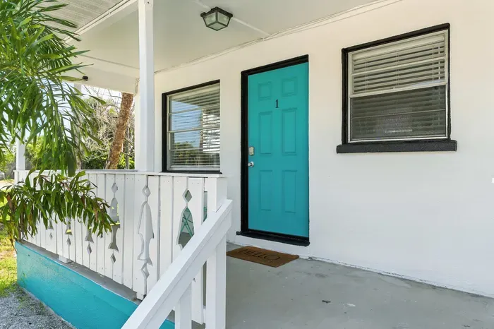 Step into your coastal escape through a vibrant turquoise door framed by crisp white walls and charming porch details. This inviting entryway sets the perfect tone for a relaxing beachside getaway.