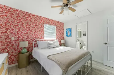 Chic bedroom with a vibrant red floral accent wall, plush white bedding, and cozy décor. Ceiling fan and en-suite bath add comfort and convenience, making it a stylish retreat for rest and relaxation.