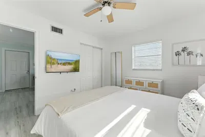 Relax in this sunlit bedroom featuring crisp white décor, a comfy bed, and modern touches. Enjoy the flat-screen TV, ceiling fan, and serene vibes—perfect for unwinding after a day of coastal adventures.