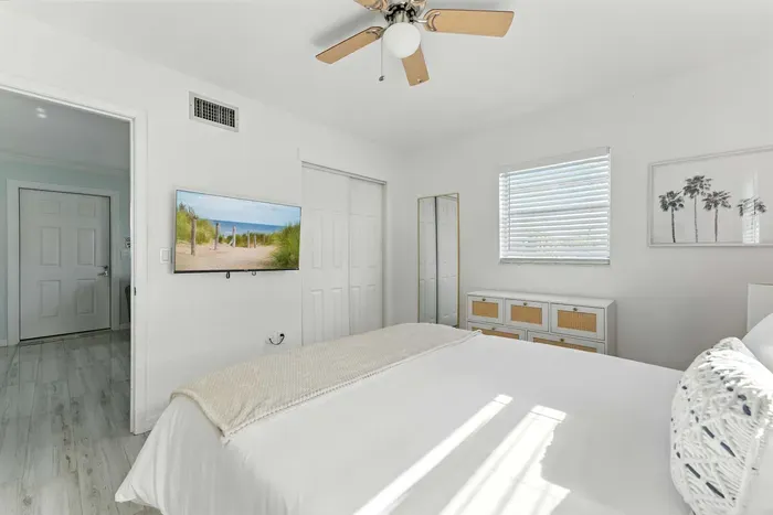 Relax in this sunlit bedroom featuring crisp white décor, a comfy bed, and modern touches. Enjoy the flat-screen TV, ceiling fan, and serene vibes—perfect for unwinding after a day of coastal adventures.