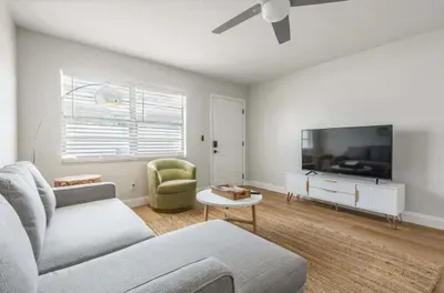 Bright and airy living room with a comfy sectional, modern décor, and large TV for entertainment. Natural light fills the space, creating a relaxing atmosphere perfect for lounging or movie nights.