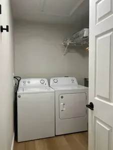 Convenient laundry room featuring a full-size washer and dryer, sleek shelving for storage, and clean neutral tones. Perfect for keeping your wardrobe fresh and ready during your stay—practical, tidy, and easy to use.