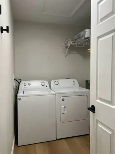 Convenient laundry room featuring a full-size washer and dryer, sleek shelving for storage, and clean neutral tones. Perfect for keeping your wardrobe fresh and ready during your stay—practical, tidy, and easy to use.