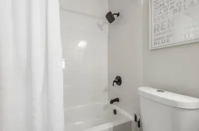 Crisp and modern bathroom with a pristine white tub and shower combo, matte black fixtures, and a fresh white curtain. Clean lines and simple décor create a relaxing, spa-like atmosphere—perfect for unwinding after a long day.