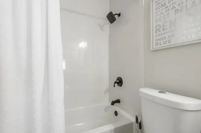 Crisp and modern bathroom with a pristine white tub and shower combo, matte black fixtures, and a fresh white curtain. Clean lines and simple décor create a relaxing, spa-like atmosphere—perfect for unwinding after a long day.