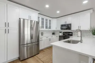Sleek and stylish kitchen with bright white cabinetry, stainless steel appliances, and quartz countertops. Perfectly equipped for cooking or entertaining, with a modern backsplash and plenty of prep space.