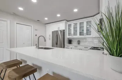 Modern kitchen with bright white finishes, quartz countertops, and sleek stainless steel appliances. Enjoy casual dining at the spacious breakfast bar with chic wooden stools.