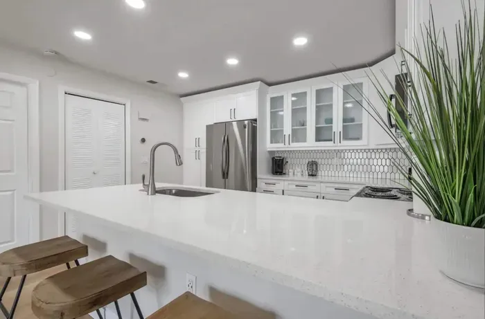 Modern kitchen with bright white finishes, quartz countertops, and sleek stainless steel appliances. Enjoy casual dining at the spacious breakfast bar with chic wooden stools.