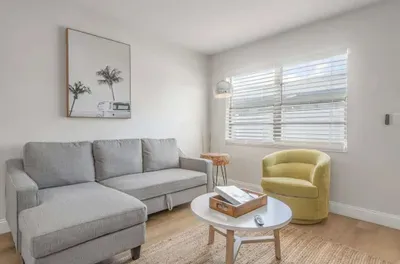 Cozy and sunlit living room featuring a plush sectional, modern décor, and stylish accent chair. Relax with natural light streaming in, perfect for unwinding or enjoying a quiet morning coffee.