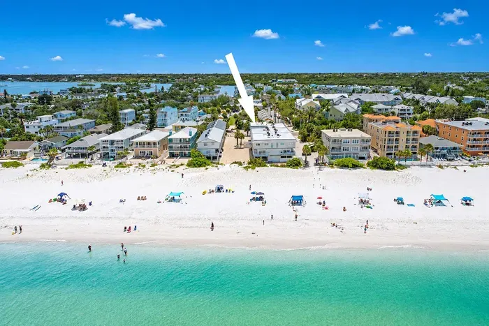 Wade in from the shore and look back — the villa, just past the sand. The neighborhood stays low-rise, so the view stays wide.