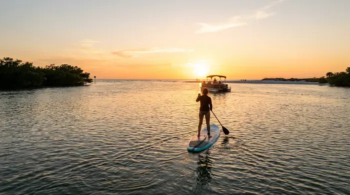 Paddleboarder enjoys a sunset with a boat in the background