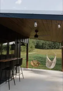 Relax on the outdoor patio featuring a swing chair, fire pit, lounger, wicker chair, and live edge wood countertop and barstools