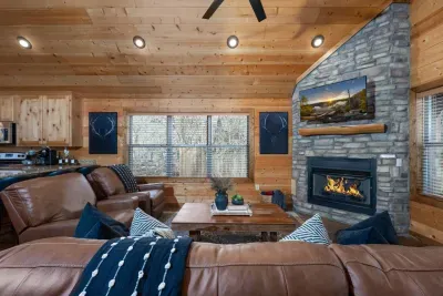 Living Room: Stylish space with plush leather seating, a stone fireplace, and scenic views.