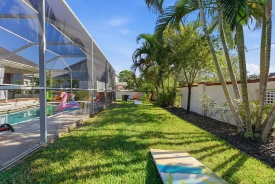 Wander the fenced side yard along the pool enclosure, shaded by palms and completely private