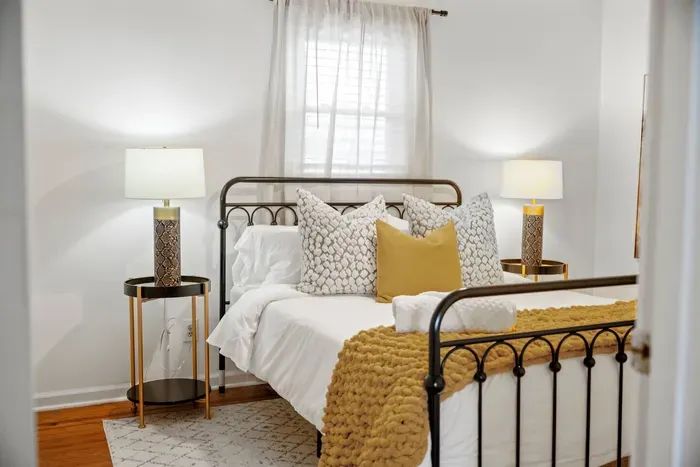 Bright, stylish bedroom with iron bed, plush linens, and cozy throw.