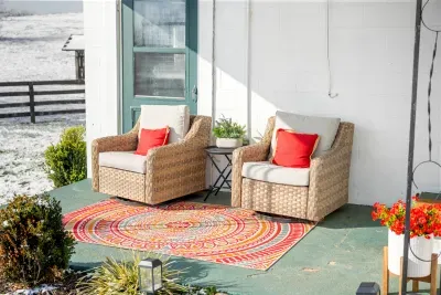 Sunny country porch with cozy chairs, vibrant rug, and pasture views.
