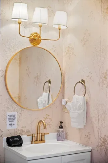 Elegant powder room with gold fixtures, round mirror, plush towels