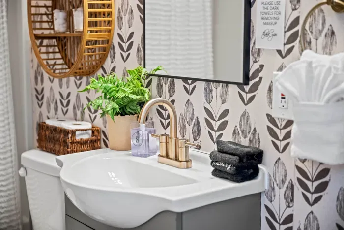 Stylish bath with brass fixtures, leafy wallpaper & plush towels