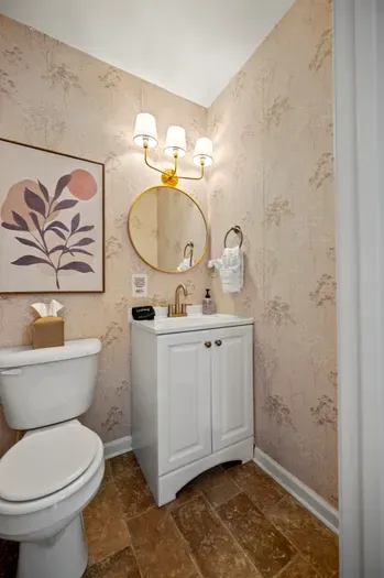 Chic powder room with brass accents, botanical wallpaper, warm lighting.