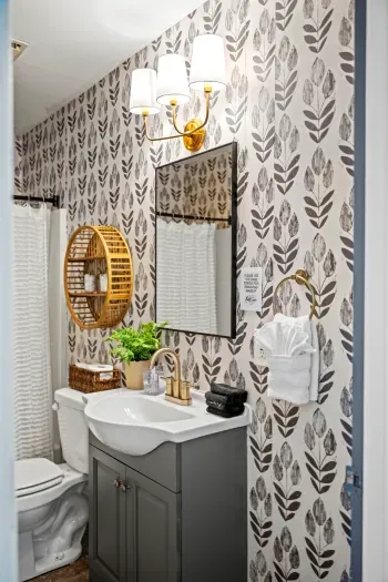 Chic bath with gold fixtures, bold wallpaper, and hotel-style amenities.