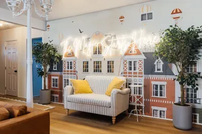 Stylish living room with a cozy sofa, unique mural backdrop, and warm neon lighting—perfect for relaxing, taking photos, and enjoying a modern, playful atmosphere.