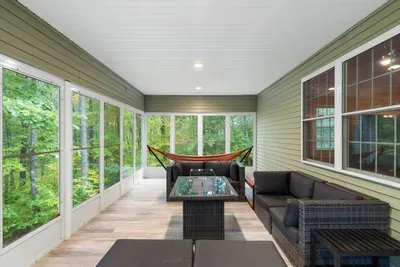 Relax on this warm, enclosed winter porch featuring comfy seating, a hammock, and forest views—perfect for skiers, families, and couples to unwind after a chilly day on the slopes or holiday adventures.