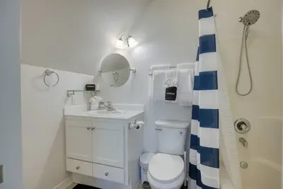 The upstairs ensuite full bathroom features a bright vanity, a large round mirror, and a clean shower/tub combo. Conveniently attached to the 2nd bedroom upstairs and fully stocked with fresh towels for your stay