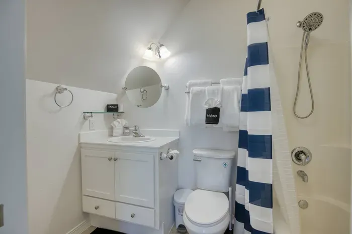 The upstairs ensuite full bathroom features a bright vanity, a large round mirror, and a clean shower/tub combo. Conveniently attached to the 2nd bedroom upstairs and fully stocked with fresh towels for your stay
