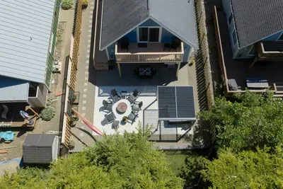 A bird's-eye view of your private backyard oasis! See the spacious patio layout featuring the pergola-shaded hot tub, outdoor dining table with seating for 6, BBQ and fully fenced yard, plus the upper-level balcony and sitting area.