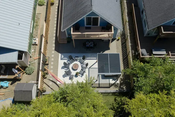 A bird's-eye view of your private backyard oasis! See the spacious patio layout featuring the pergola-shaded hot tub, outdoor dining table with seating for 6, BBQ and fully fenced yard, plus the upper-level balcony and sitting area.
