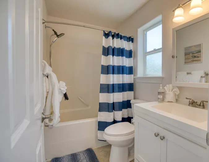 The main floor full bathroom features a clean vanity, a large mirror, bright lighting, and a full shower/tub combo. Fully stocked with fresh, plush bath towels for your convenience.