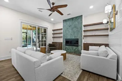 Refined coastal living room anchored by a striking green statement fireplace, warm wood built-ins, and layered textures. Comfortable seating invites gathering, with easy access to the porch for seamless indoor-outdoor living.