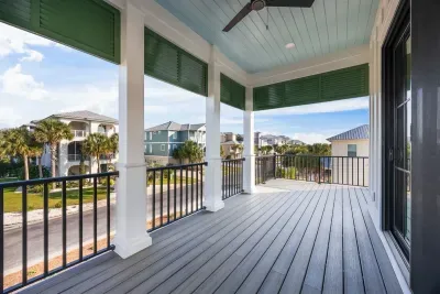 A serene upper porch retreat off the primary suite, framed by classic columns and haint blue ceilings, offering peaceful neighborhood views and the perfect setting for morning coffee or quiet evening unwinding.