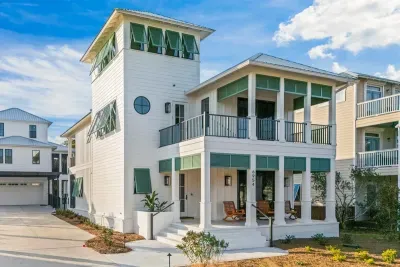 Magnolia Mooring — a light-filled coastal retreat with classic white siding, breezy double porches, and signature green shutters, perfectly positioned in the heart of Kiva Dunes just a short walk to the beach.