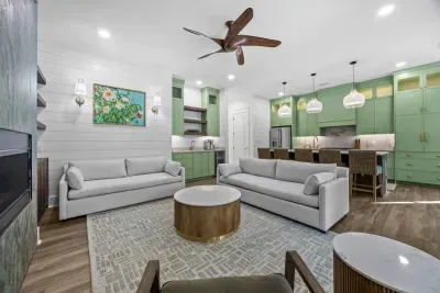An elegant coastal living space with custom green cabinetry, warm wood tones, and tailored furnishings, anchored by a refined kitchen and open layout—thoughtfully designed for comfort, conversation, and effortless indoor-outdoor flow.