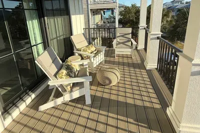 A gracious covered porch designed for slow coastal mornings and golden-hour evenings, with Adirondack seating, soft cushions, and open sightlines that invite the Gulf breeze to move effortlessly through the space.