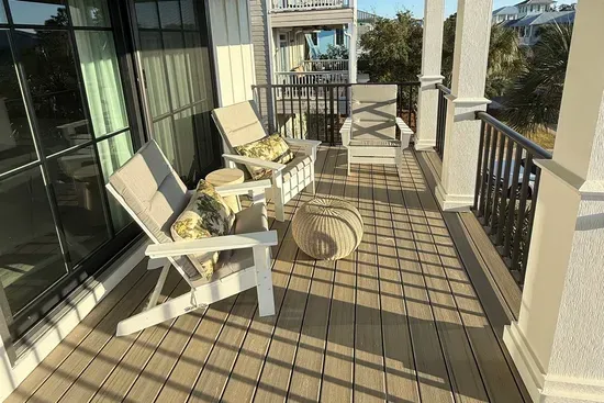 A gracious covered porch designed for slow coastal mornings and golden-hour evenings, with Adirondack seating, soft cushions, and open sightlines that invite the Gulf breeze to move effortlessly through the space.